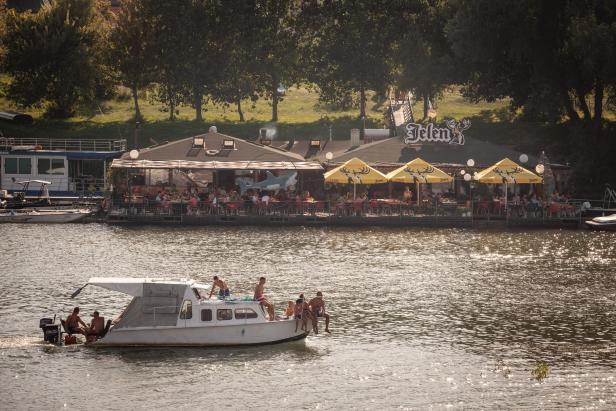 Ein Ausflugsboot fährt auf einem Fluss an einem schwimmenden Restaurant vorbei.