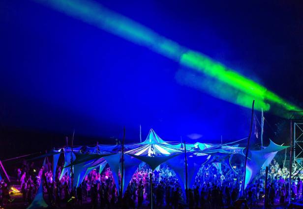 Menschen feiern unter einem Zelt mit blauem Licht und grünen Laserstrahlen.