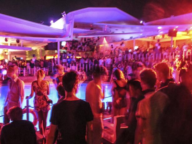Menschen feiern in einem Pool unter farbiger Beleuchtung.