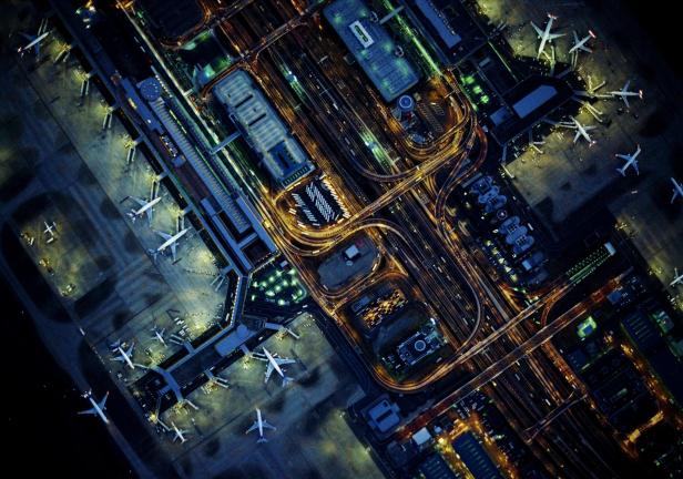 Luftaufnahme des beleuchteten Flughafens Tokio-Haneda bei Nacht.