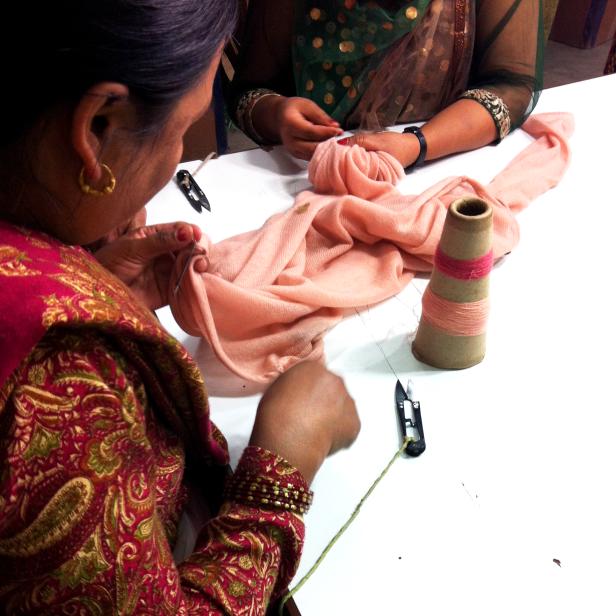 Zwei Frauen arbeiten an einem hellrosa Stoff mit Nadel und Faden.