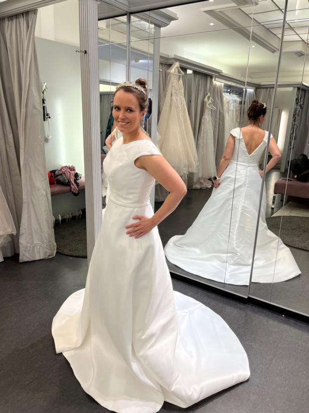 Eine Frau probiert in einem Geschäft ein weißes Brautkleid mit Schleppe an.