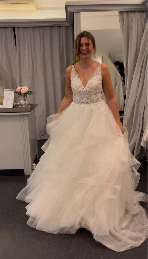 Eine lächelnde Frau in einem weißen Brautkleid mit Spitze und Tüll.