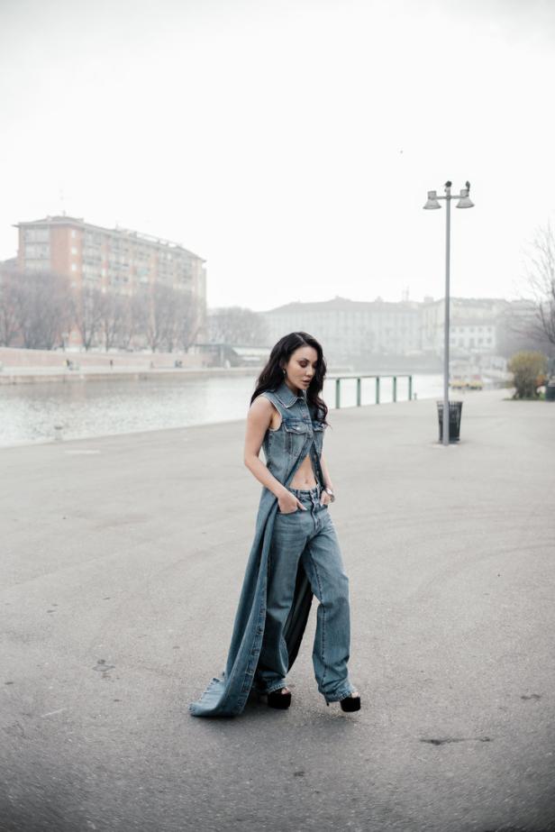Eine Frau in einem Jeans-Outfit posiert am Ufer eines Flusses.