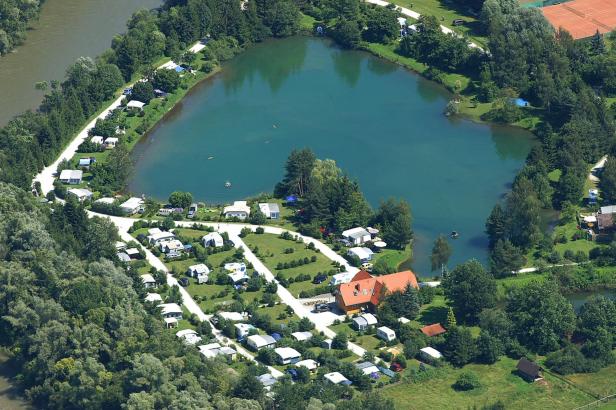Luftaufnahme eines Campingplatzes am Ufer eines Sees, auf dem auch geschwommen wird.