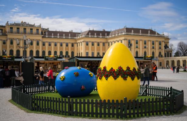 Ostermarkt vor Schloss Schönbrunn: Es stehen zwei riesige, bunte Ostereier, ein gelbes und ein blaues, umzäunt von einem kleinen Zaun.