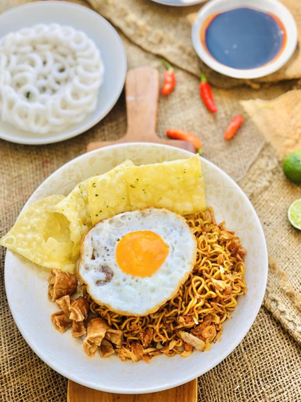 Gebratene Nudeln mit Spiegelei, Krabbenchips und Sojasauce auf einem Tisch.