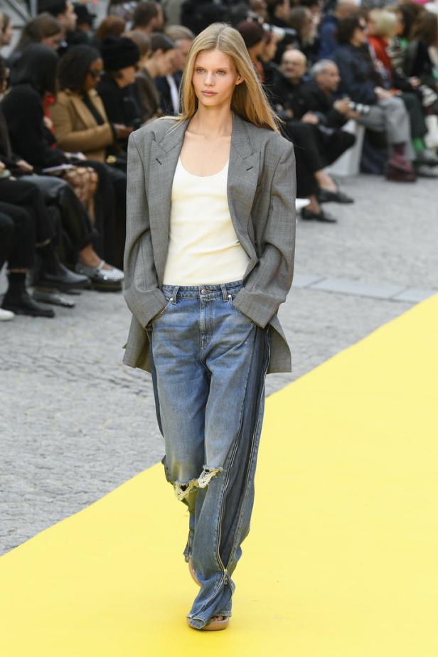 Ein Model präsentiert ein Outfit mit übergroßem Blazer und Jeans mit Reißverschlüssen auf dem Laufsteg.