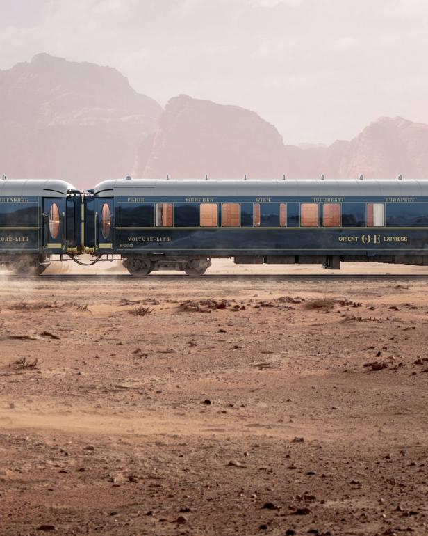 Der Orient-Express fährt durch eine Wüstenlandschaft mit Bergen im Hintergrund.