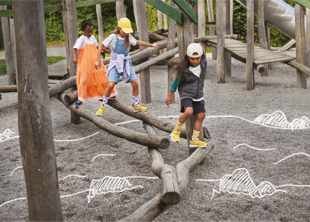 Drei Kinder balancieren auf einem Baumstamm-Spielplatz.