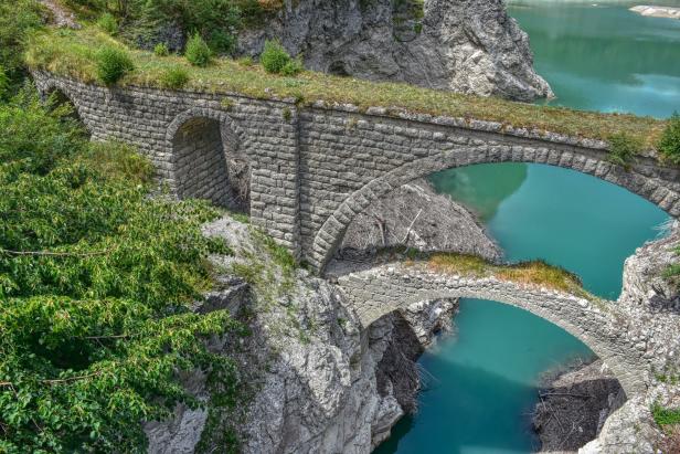 Eine alte Steinbrücke überspannt türkisfarbenes Wasser.
