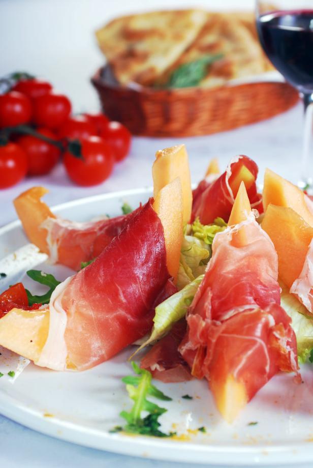 Ein Teller mit Melone und Schinken, garniert mit Salat und Tomaten.