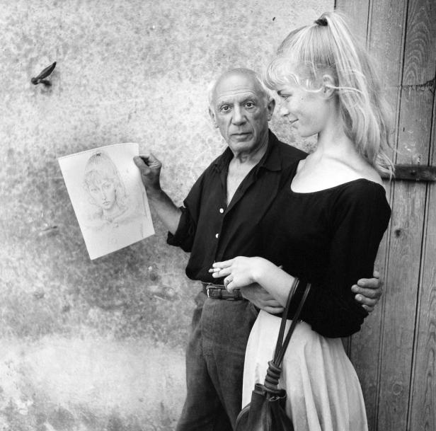 Pablo Picasso mit einer jungen Frau und einer Porträtzeichnung in der Hand.