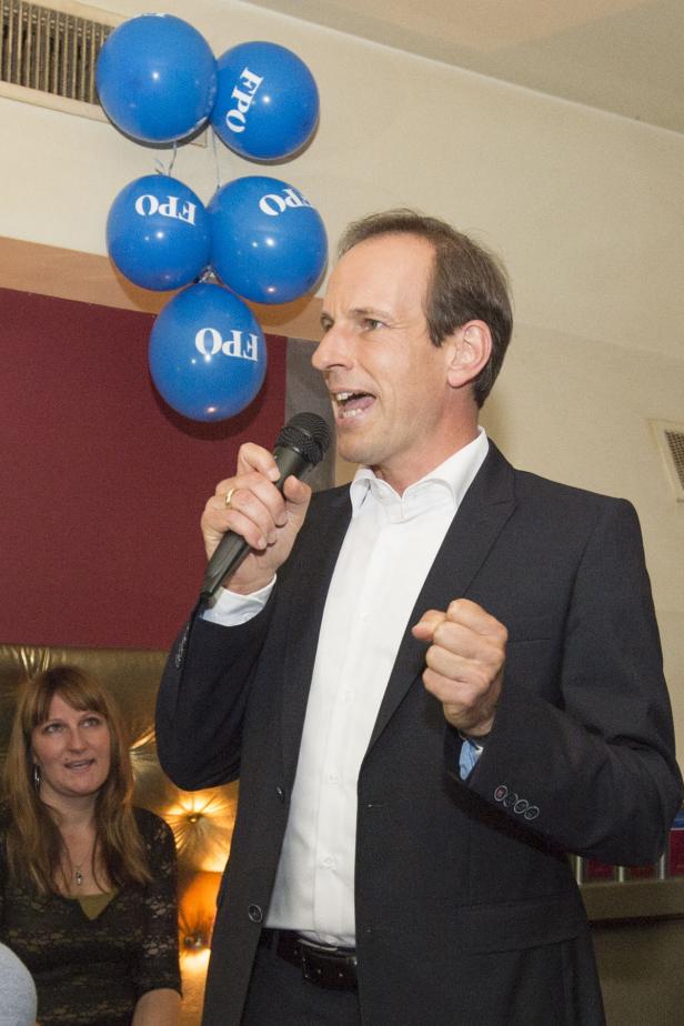 Ein Mann im Anzug spricht in ein Mikrofon vor blauen FPÖ-Luftballons.