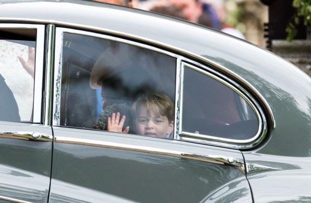 Prinz George winkt aus dem Fenster eines grauen Autos.