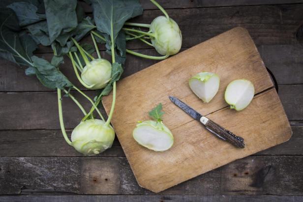 Bio-Kohlrabi mit Messer und Schneidebrett auf einem Holztisch.