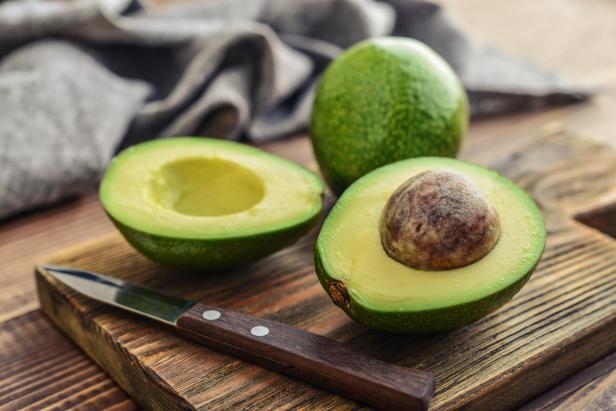 Eine ganze und zwei halbe Avocados liegen auf einem Holzbrett.