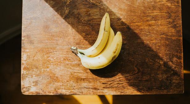 Drei Bananen liegen auf einem Holztisch.