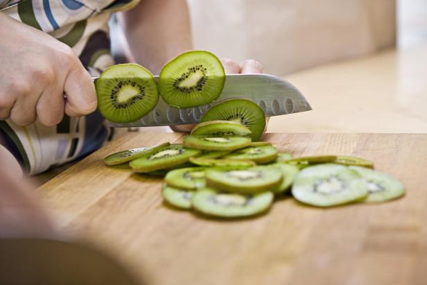 Eine Hand schneidet Kiwis auf einem Holzbrett.