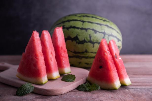 Wasserscheiben und eine ganze Wassermelone auf einem Holzbrett.