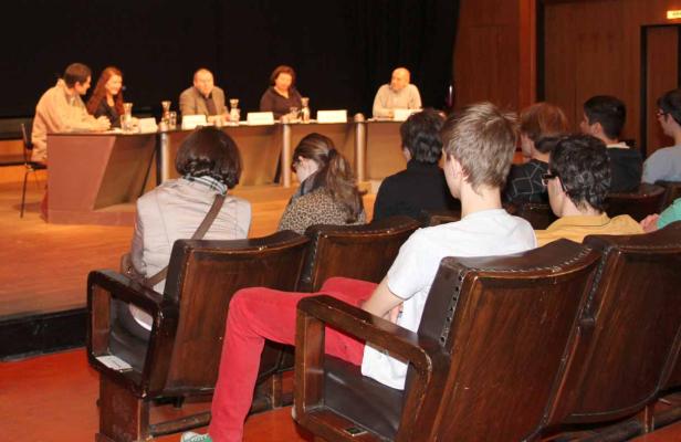 Zuschauer sitzen in einem Theatersaal vor einer Podiumsdiskussion.