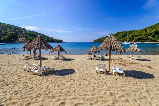 Ein sonniger Strand mit Strohschirmen und Liegestühlen lädt zum Verweilen ein.