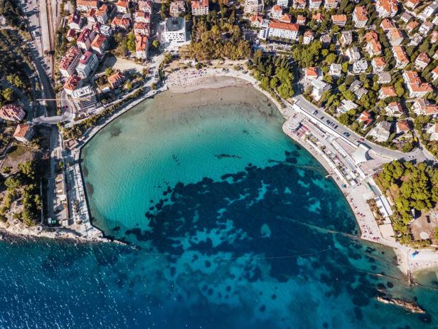Luftaufnahme einer Küstenstadt mit einem Strand und türkisfarbenem Wasser.