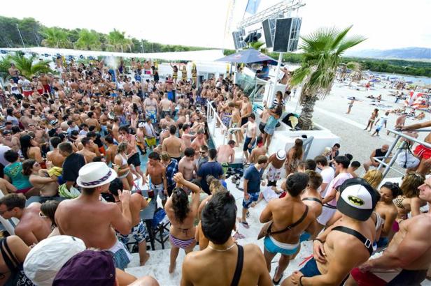 Eine große Menschenmenge feiert auf einer Strandparty mit Musik und Tanz.