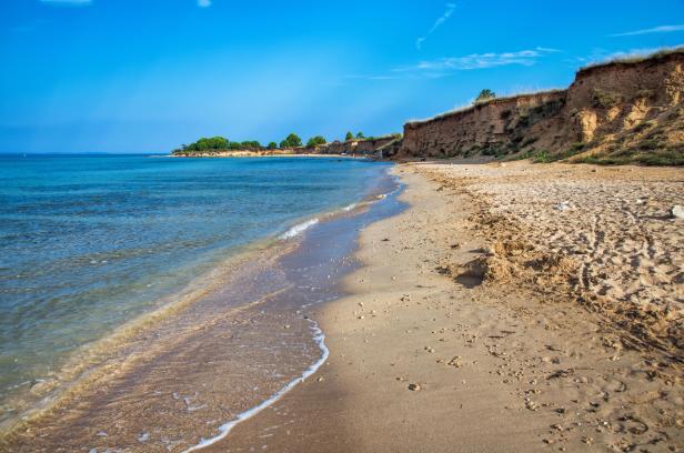 Ein Sandstrand mit einer kleinen Klippe unter blauem Himmel.