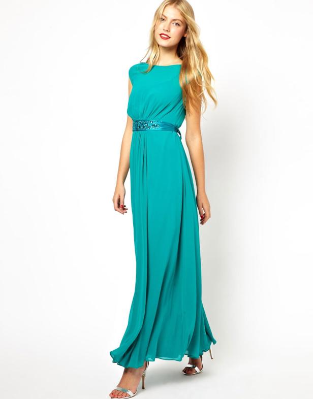 Eine blonde Frau trägt ein langes, türkisfarbenes Kleid mit einem verzierten Gürtel.