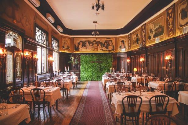 Innenansicht eines eleganten Restaurants mit gedeckten Tischen und Wandmalereien.