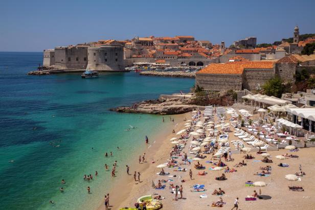 Ein belebter Strand in Dubrovnik mit Badegästen und Blick auf die Altstadt.
