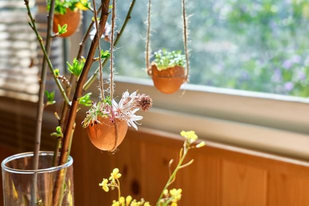 Dekorative Ostereier mit Pflanzen und Blumen hängen vor einem Fenster.