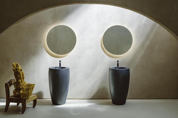 Ein Badezimmer mit zwei runden Spiegeln über freistehenden Waschbecken und einem Stuhl mit einem Schwamm darauf.