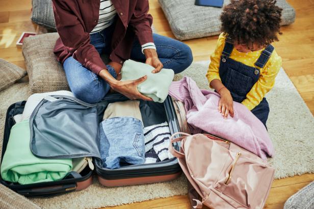 Ein kleines afroamerikanisches Mädchen hilft seiner Mutter, ihren Koffer zu packen.