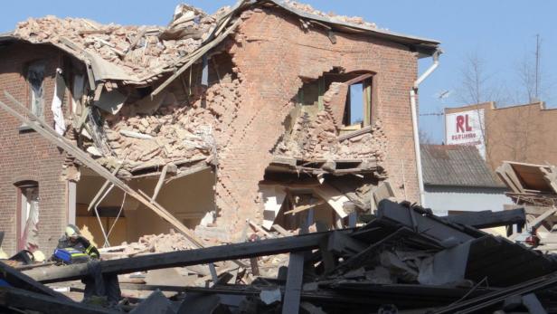 Ein durch eine Explosion zerstörtes Backsteingebäude mit einem Feuerwehrmann vor den Trümmern.