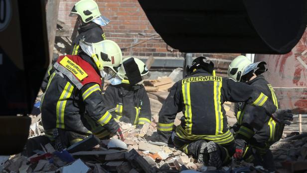 Mehrere Feuerwehrleute räumen Trümmer nach einem Gebäudezusammenbruch beiseite.