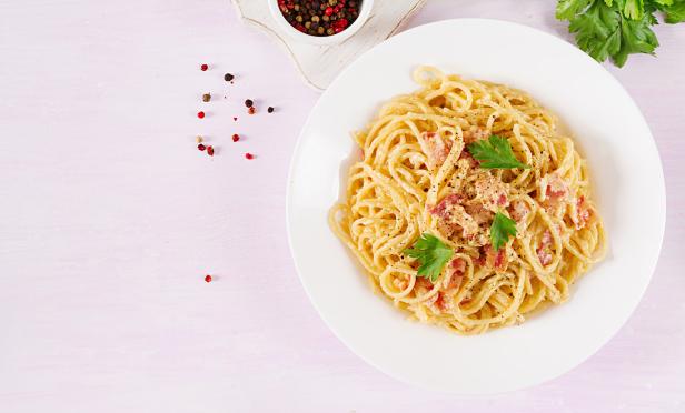Ein Teller Spaghetti Carbonara, garniert mit Petersilie, steht auf einem Tisch.