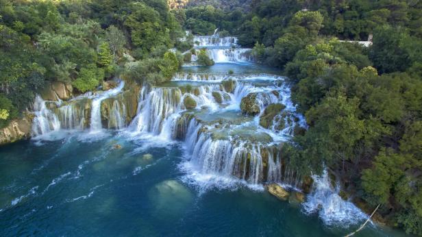 Mehrere Wasserfälle stürzen über Felsen in einen türkisfarbenen Fluss.