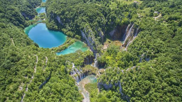 Luftaufnahme der Plitvicer Seen mit türkisfarbenem Wasser und Wasserfällen, umgeben von üppigem Grün.