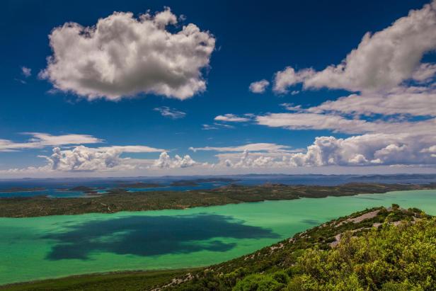 Blick auf eine grüne Bucht mit Inseln unter blauem Himmel mit Wolken.