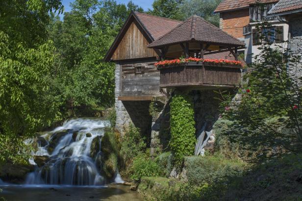 Eine alte Mühle mit einem kleinen Wasserfall im Grünen.