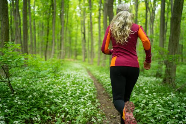 Eine Frau joggt auf einem Pfad durch einen grünen Wald voller blühender Blumen.