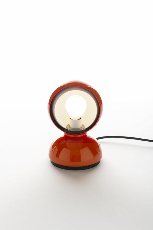 Eine orangefarbene Schreibtischlampe mit einem runden Lampenschirm und einem schwarzen Kabel.