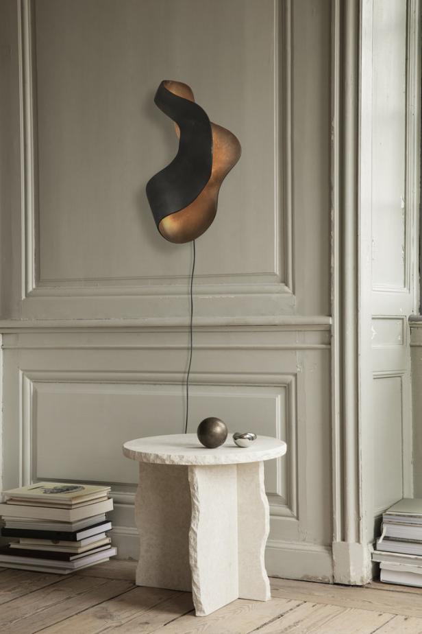 Eine moderne Wandleuchte in Form einer abstrakten Skulptur über einem kleinen Tisch.