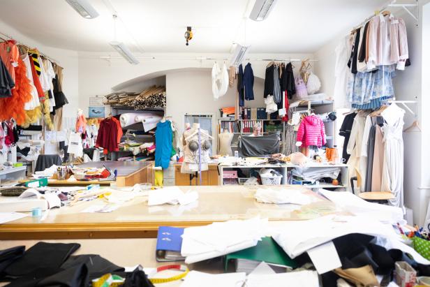 Ein Schneideratelier mit einem großen Zuschneidetisch und vielen Stoffen und Kleidungsstücken.