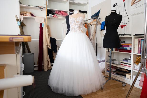 Ein weißes Brautkleid steht auf einer Schneiderpuppe in einem Atelier.