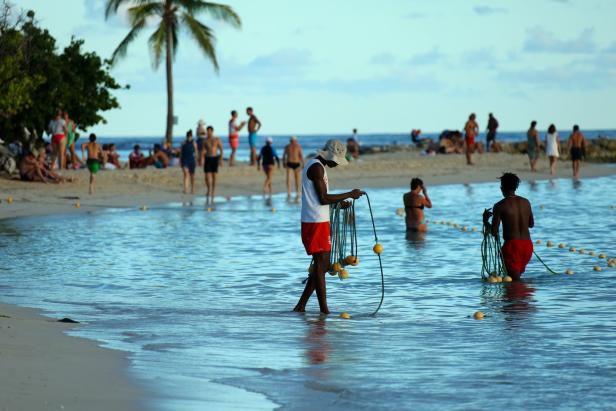 Zwei Männer ziehen eine Bojenkette durch das flache Wasser an einem Strand.