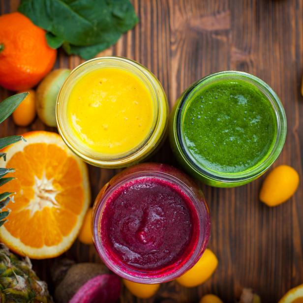 Drei Gläser mit bunten Smoothies stehen auf einem Holztisch, umgeben von frischen Früchten.