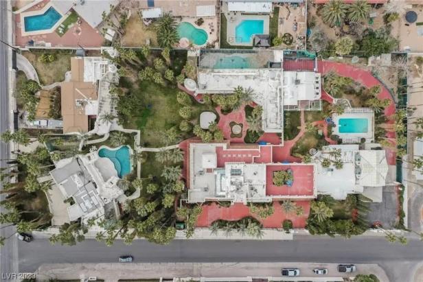 Luftaufnahme von mehreren Häusern mit Pools und üppigen Gärten entlang einer Straße.